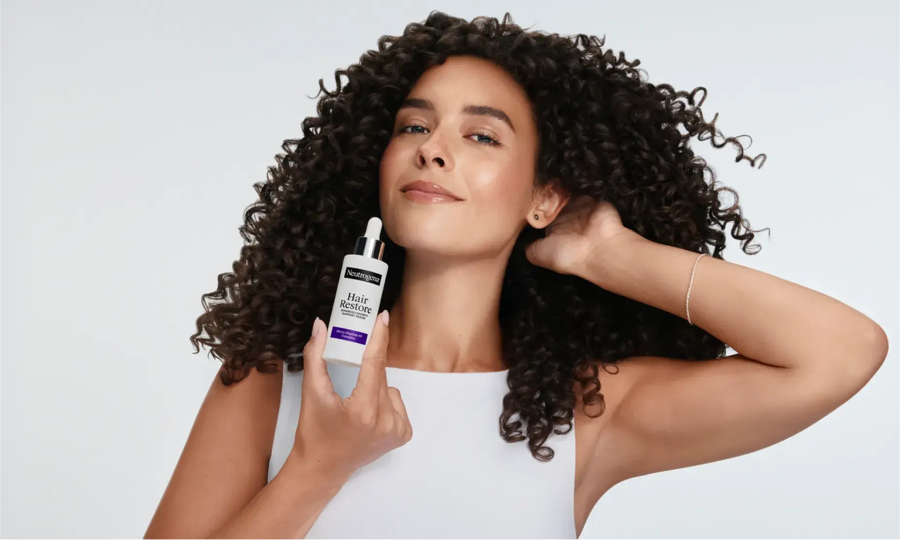 Woman with coily hair holding a bottle of Neutrogena® Hair Restore Advanced Growth Support Serum
