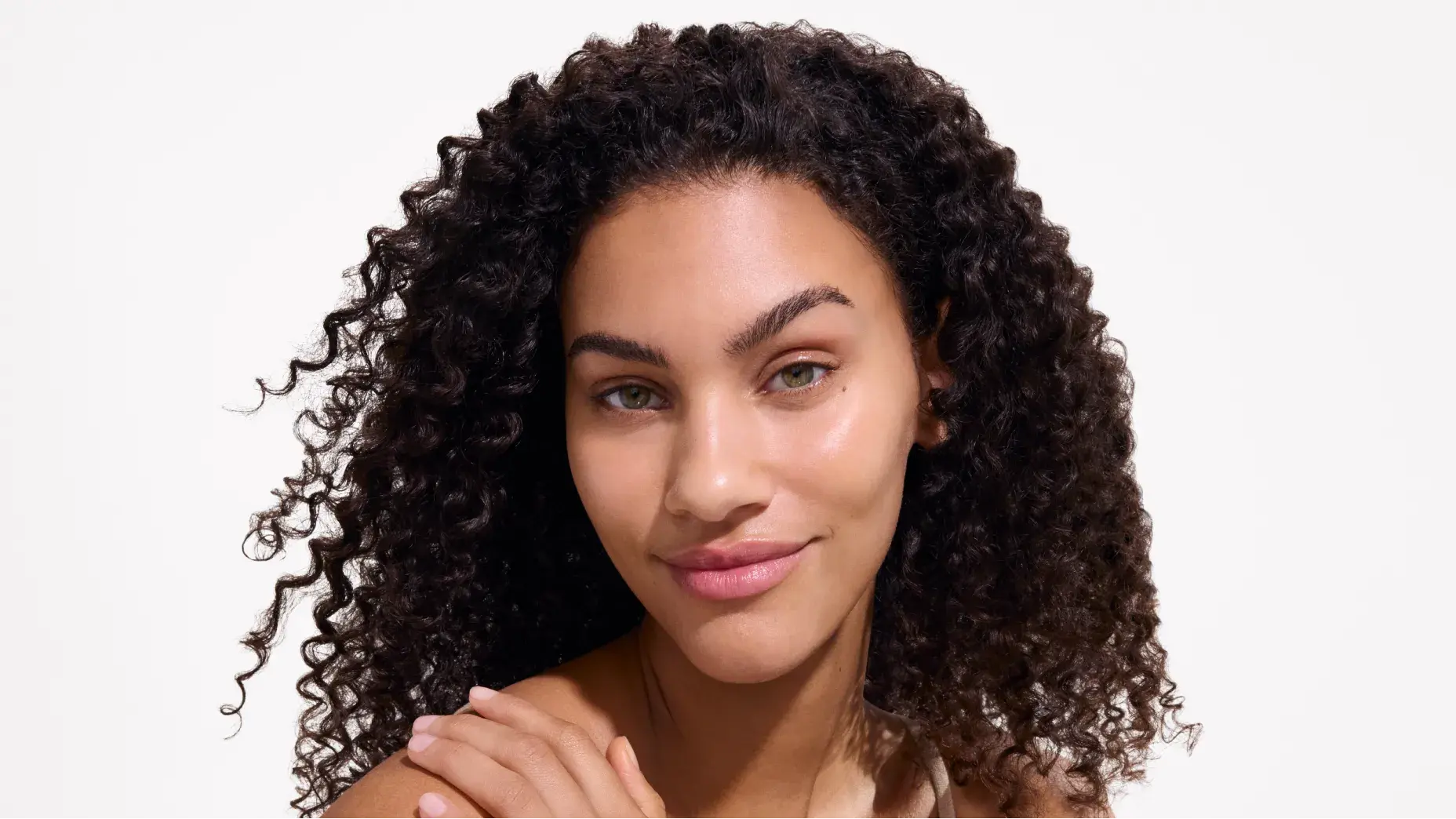 Close-up of a woman with curly hair and natural makeup, smiling softly with glowing skin after applying Neutrogena® Ultra Sheer® Sunscreen