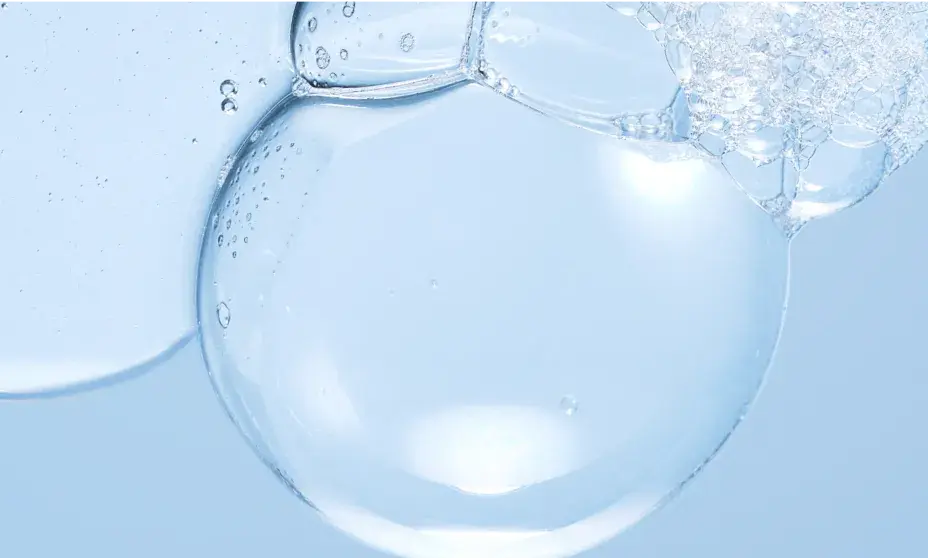 Close-up of a large, translucent water bubble surrounded by a cluster of smaller foam bubbles against a light blue background.