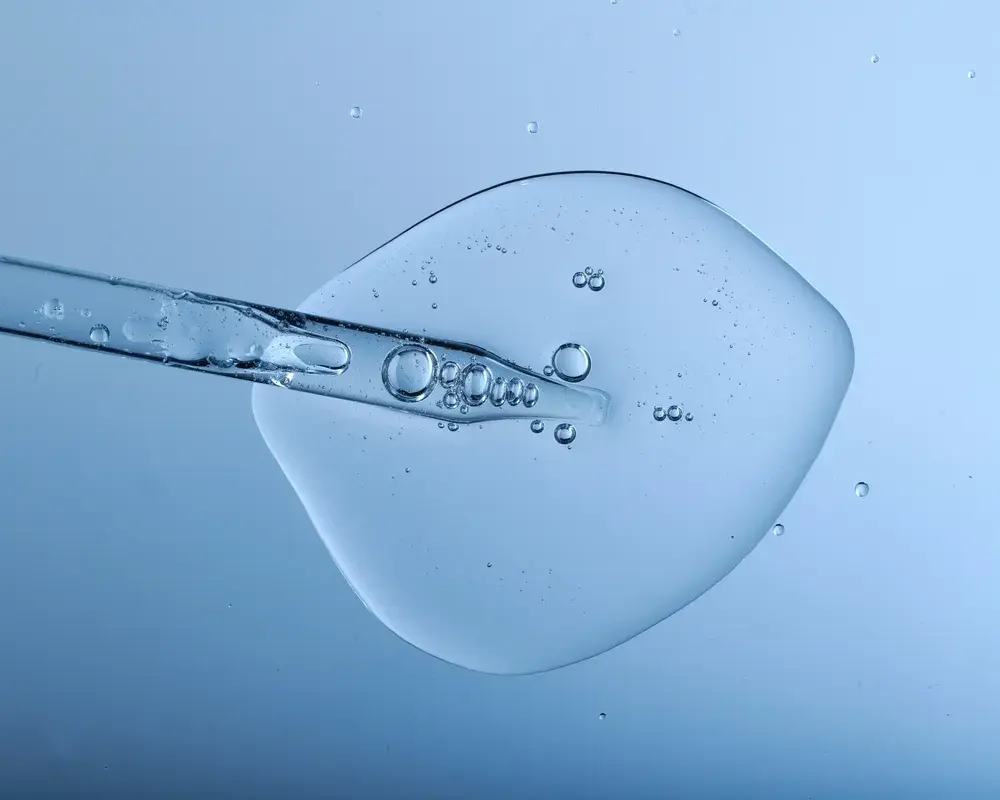 Pipette with bubbles and clear formulation being expelled. Clear liquid with bubbles resembling glycerin, hyaluronic acid or keratin in laboratory or scientific setting.