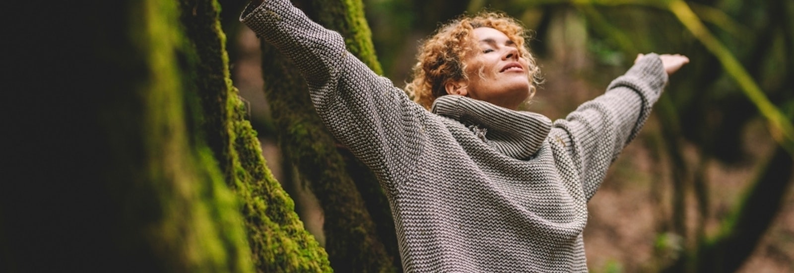 Overjoyed happy woman enjoying the green beautiful nature woods forest around her - concept of female people and healthy natural lifestyle - happiness emotion and adult lady opening arms