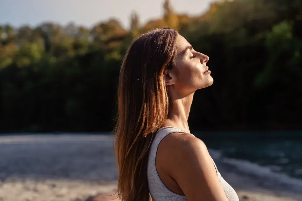 Young woman with long hair enjoying sun with closed eyes getting natural vitamin D outdoors. 