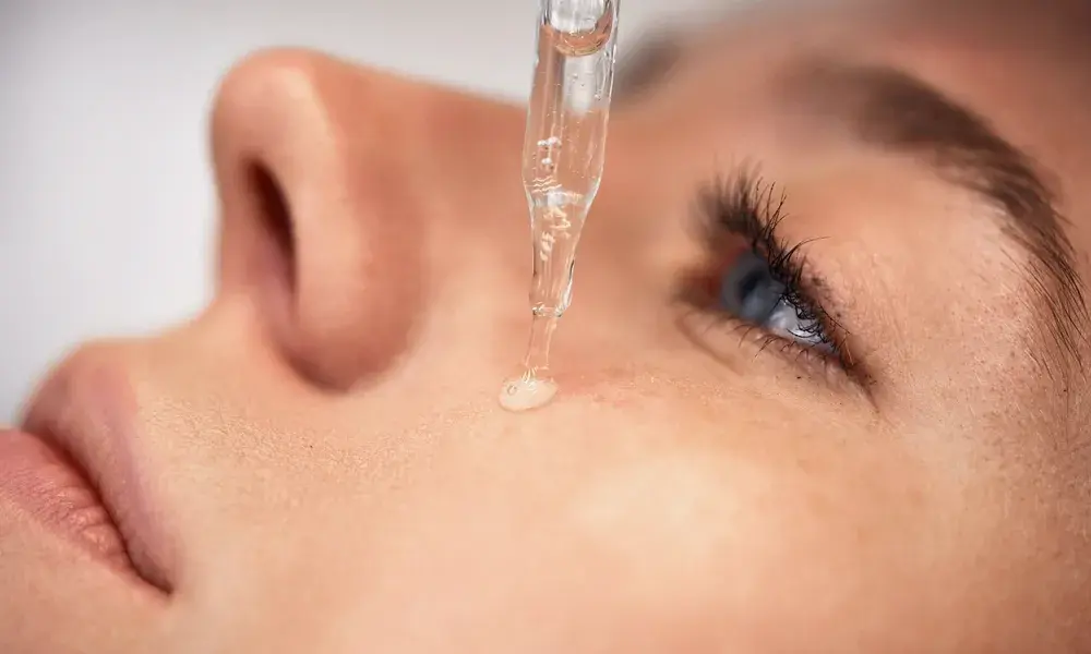 A dropper filled with clear fluid against a pink background.