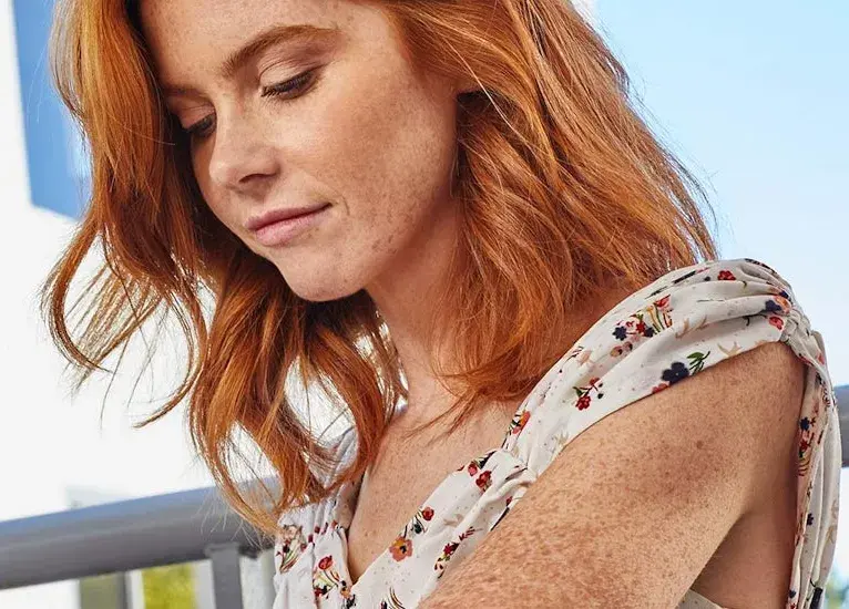 Woman with red hair and freckles looking down.