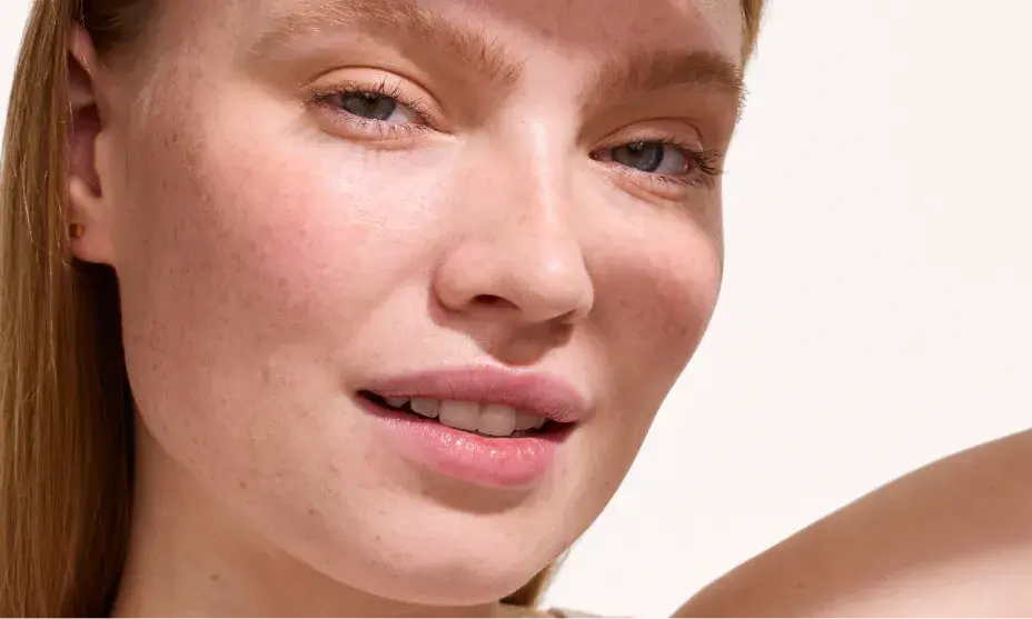Close-up portrait of a woman with light freckles and natural makeup, looking at the camera.