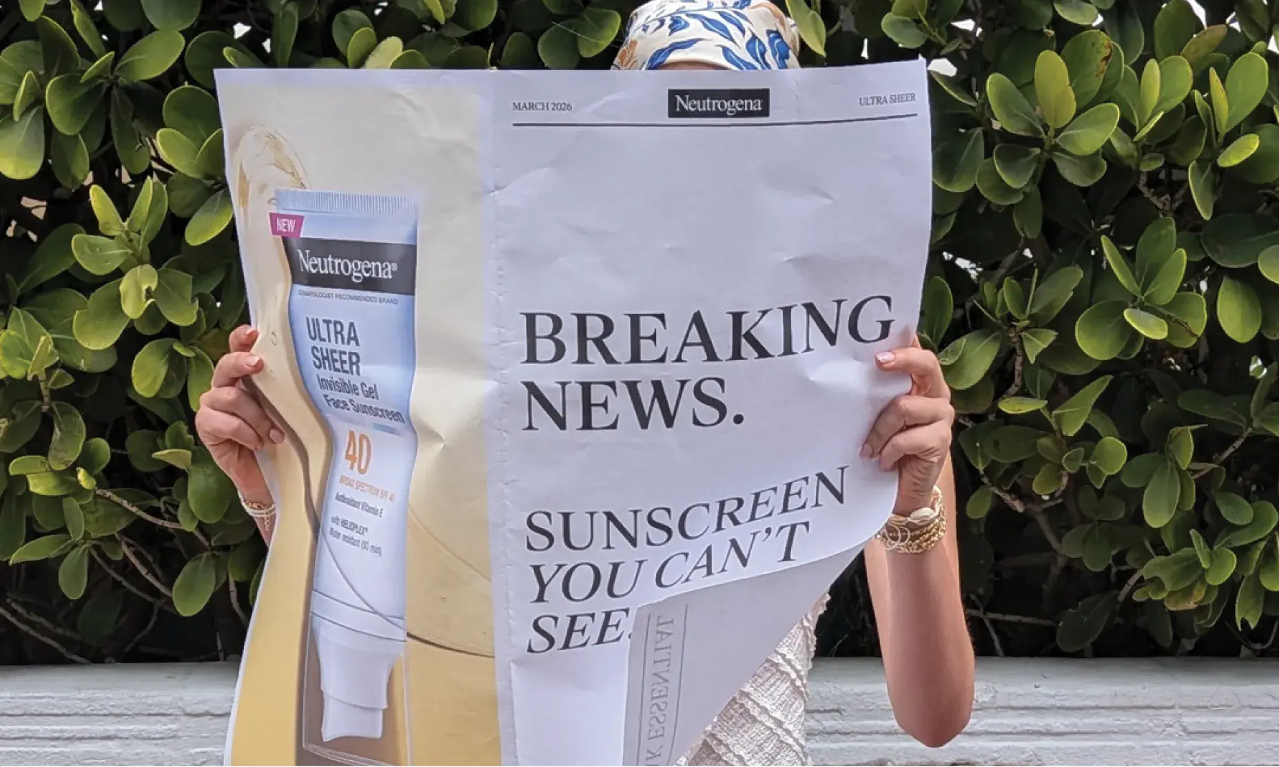Woman holding up a newspaper Neutrogena® displaying Neutrogena® Ultra Sheer® Invisibile Gel Sunscreen, and the words “Breaking News: Sunscreen You Can’t See“