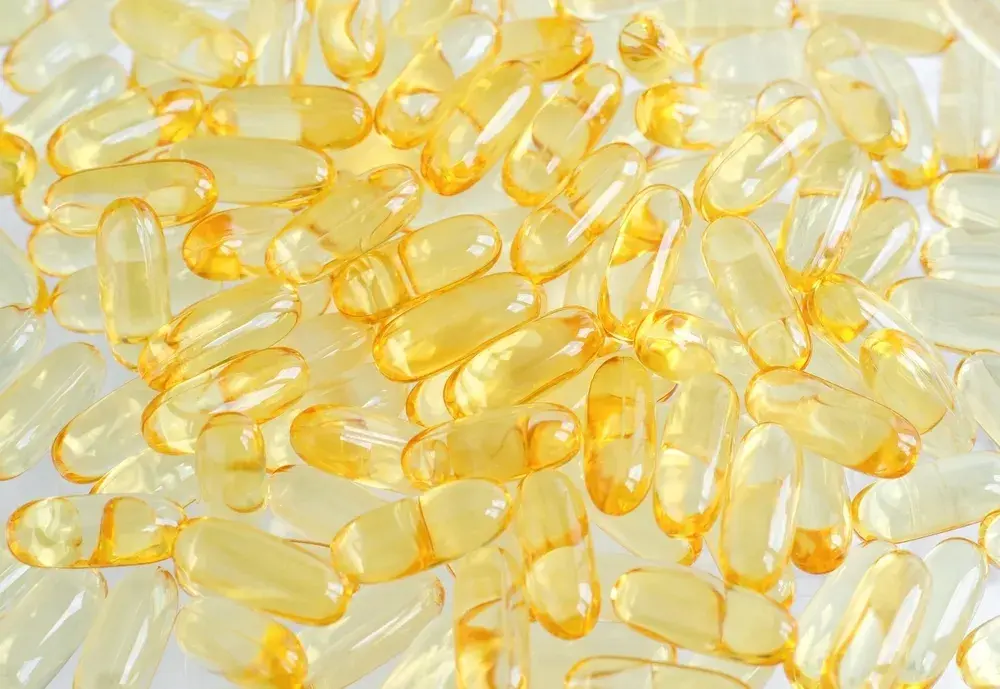 A smiling woman holds up a gel capsule filled with yellow liquid.