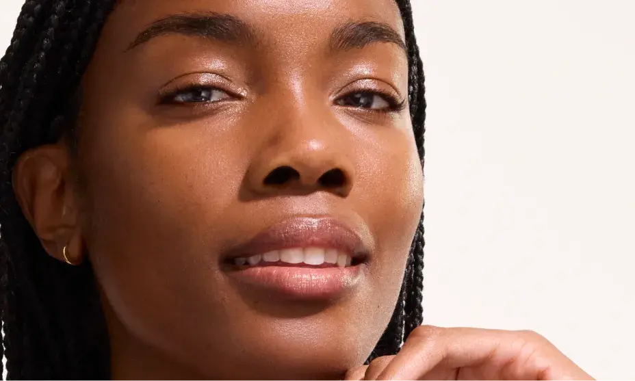 Close-up portrait of a woman with braided hair and smooth skin, gently touching her chin.