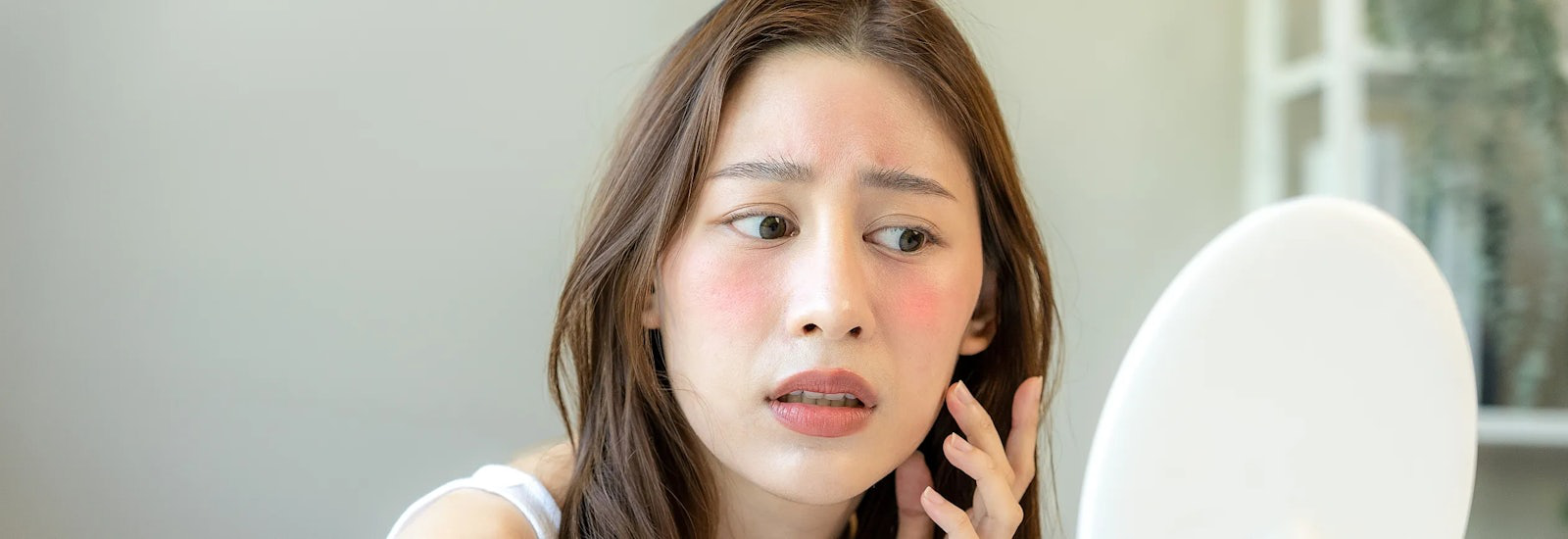 A woman looks at her skin in the mirror.