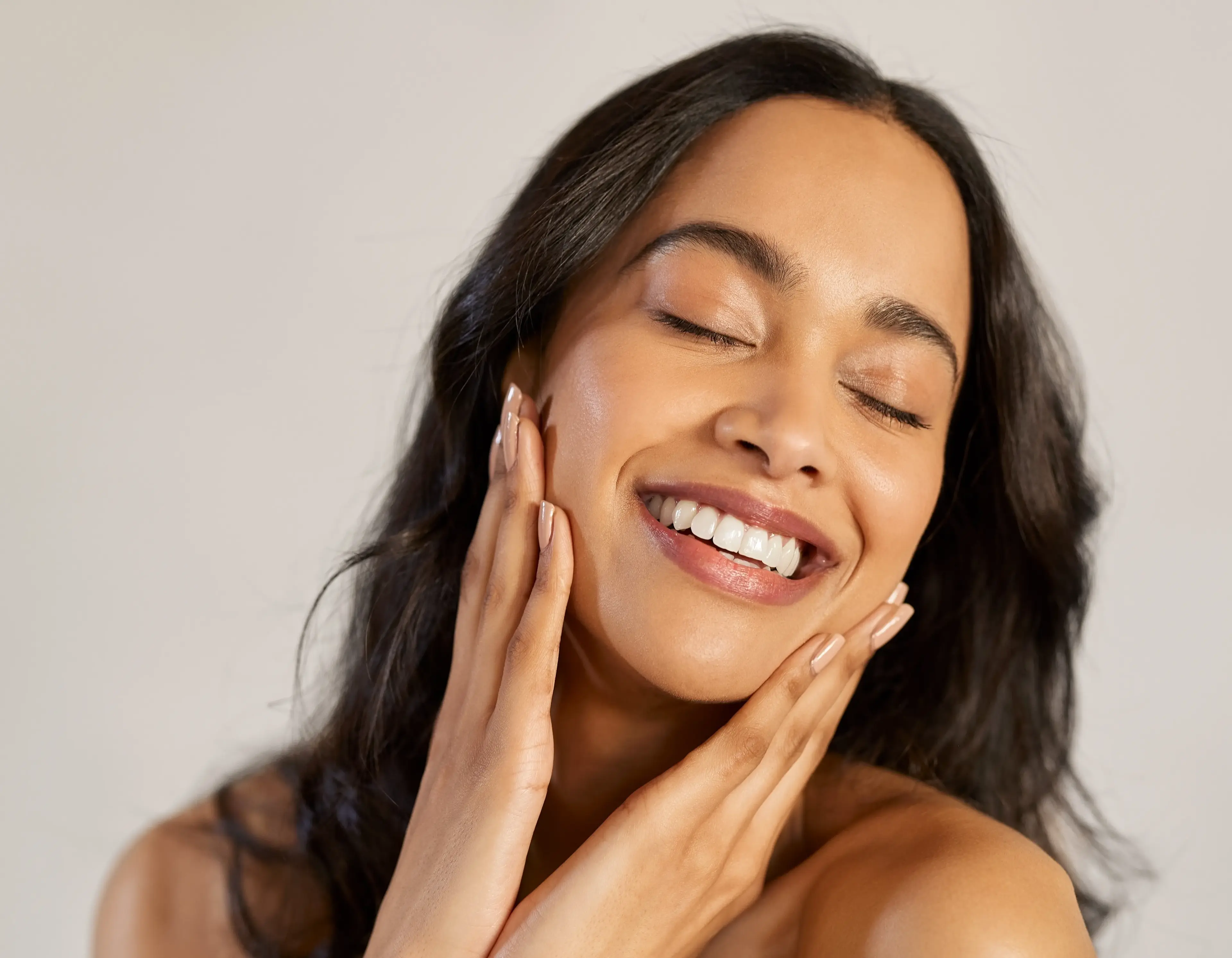 A woman smiles with her hands on either side of her face.