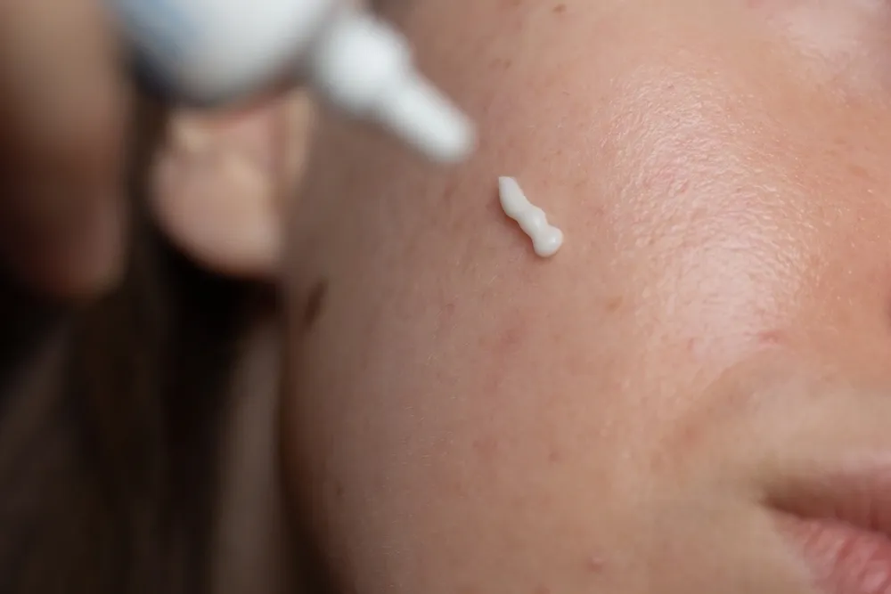 A person applies cream to their cheek. 