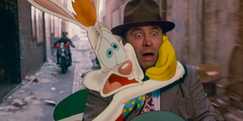 A motorcycle cop in a black uniform rides down a city alley towards the camera. In front of the cop is Roger Rabbit, a white cartoon rabbit with red hair wearing a blue and yellow bow tie, and yellow gloves, clinging on to Eddie Valiant, a white man (not a cartoon) wearing a gray suit, red and black patterned tie, and brown fedora.