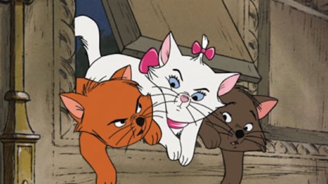 Three kittens are pushing out of a flap door in a brown wooden wall, Toulouse (an orange cat), Marie (a white cat with a pink hair bow and a pink bow collar), and Berlioz (a dark brown cat).