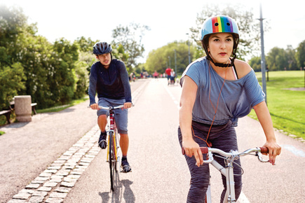 Two people biking, one wearing a rainbow helmet