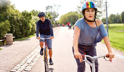 Two people biking, one wearing a rainbow helmet