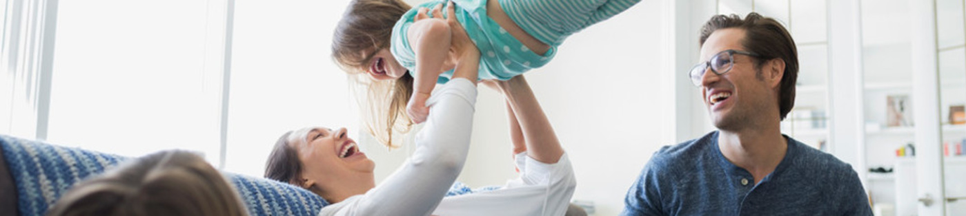 Mom lifting laughing daughter in air while father watches
