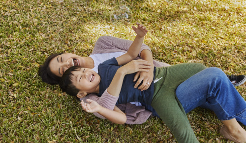 Mom hugging her child while laying on grass