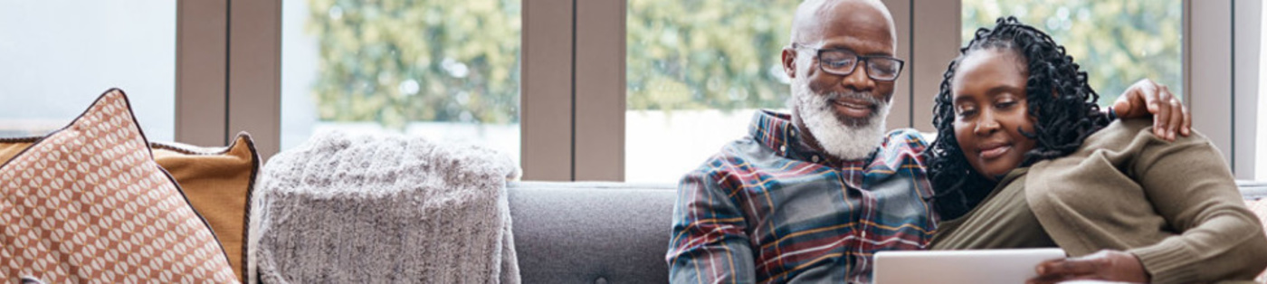 An older black couple sitting on a couch looking at a computer together