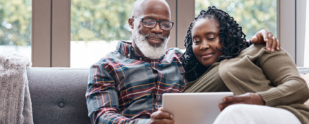 An older black couple sitting on a couch looking at a computer together