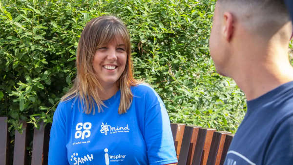 woman wearing a blue t-shirt smiling while speaking to a young man