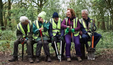 Volunteers sitting on a bench in a forest holding tools for gardening