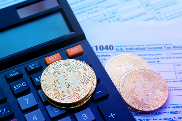Moedas de bitcoin sobre uma calculadora e algumas contas em papel representando os pagamentos em imposto de renda crypto