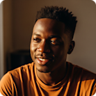 Young man with short dark hair in an orange shirt smiling softly in warm, golden lighting.