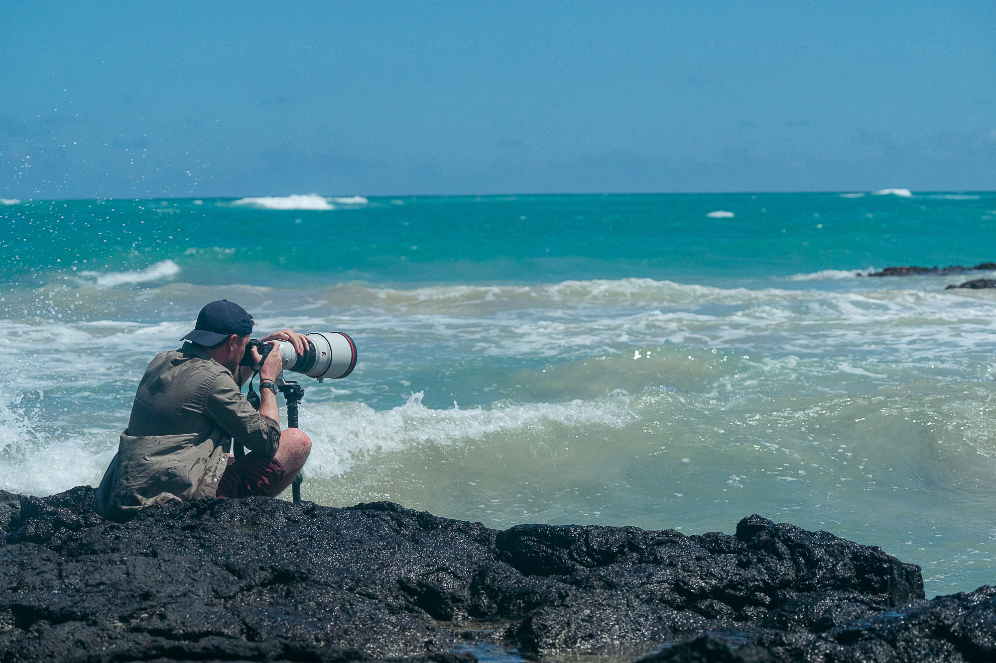 Mark Rowe sitting on rocks on The Galápagos Islands shooting with the Sony 400mm f/2.8 GM lens.