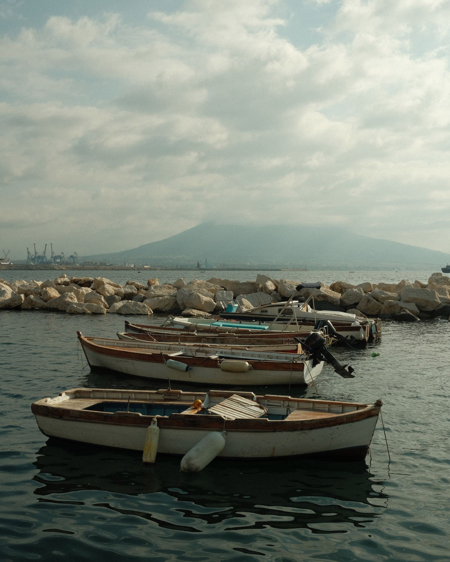 Boote in einer Reihe hintereinander auf dem Wasser, im Hintergrund der Vesuv Vulkan in den Wolken, aufgenommen von Michael Schulz mit einer Fujifilm X100V.