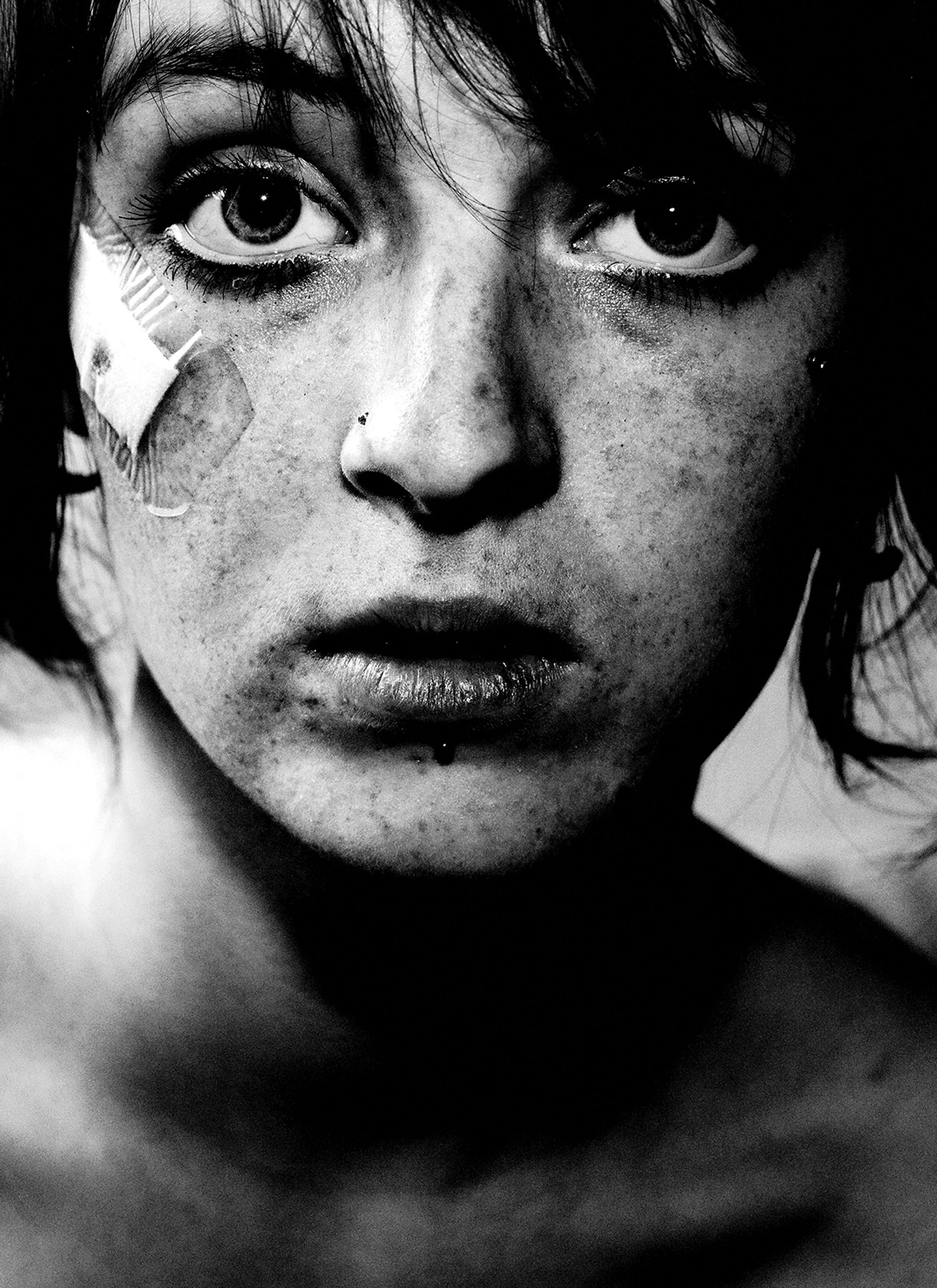 Photographie en noir et blanc d'une personne avec un sparadrap sous l'œil droit, photo de Jens Juul
