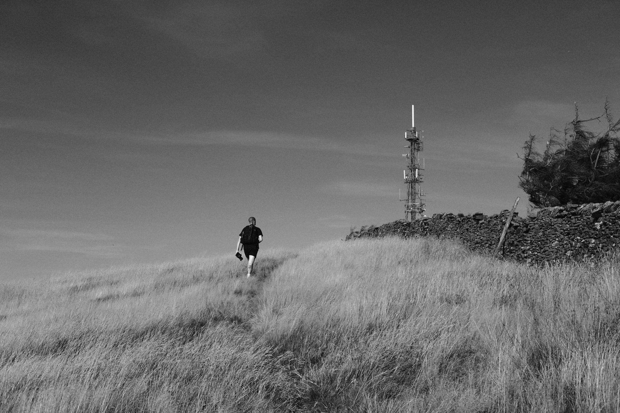 Schwarz-Weiß-Aufnahme, in der eine Person einen Hügel hinauf zu einem Strommast geht, aufgenommen von Ian Howorth mit der Fujifilm X-T3.