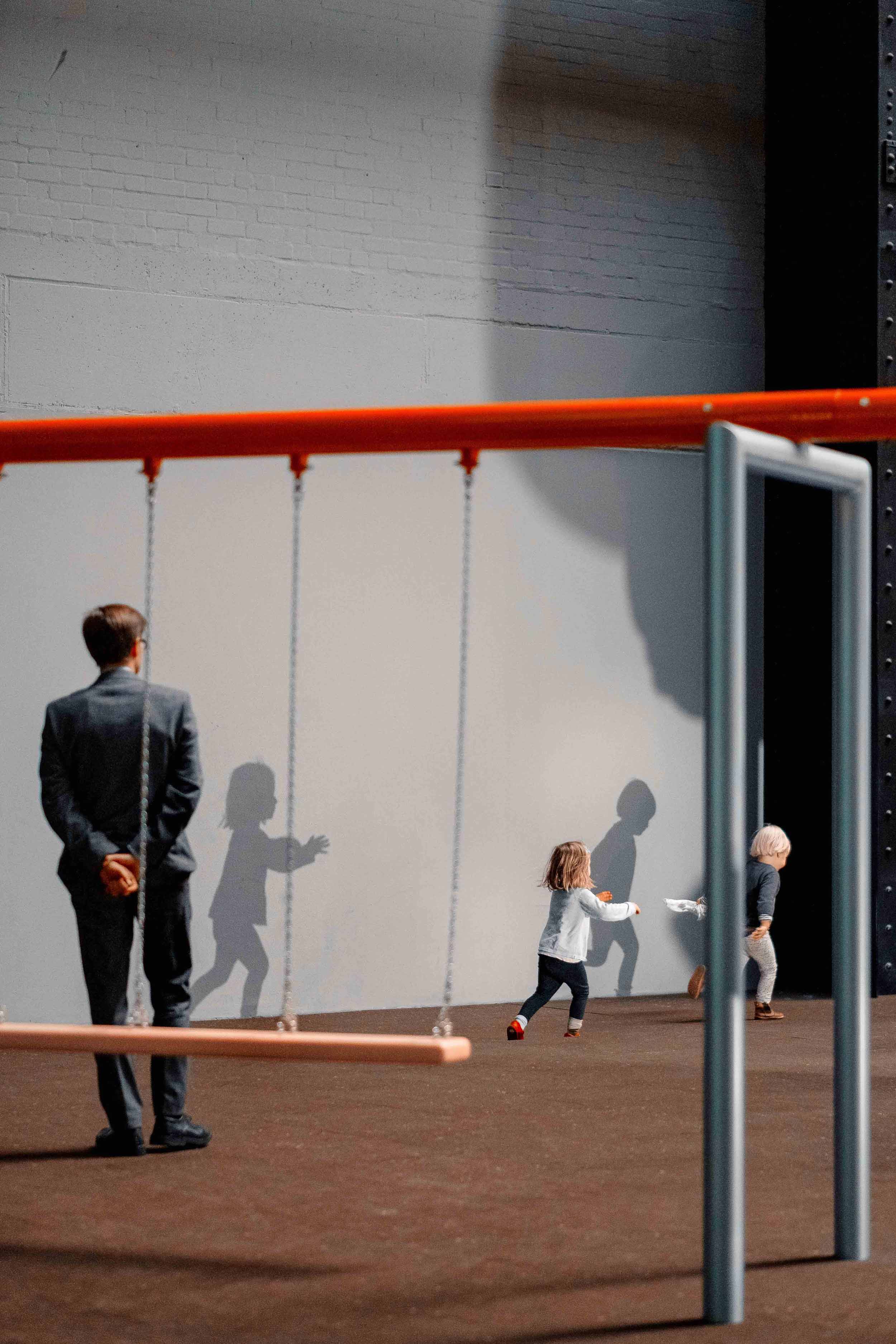 Person looks on at children playing near swings