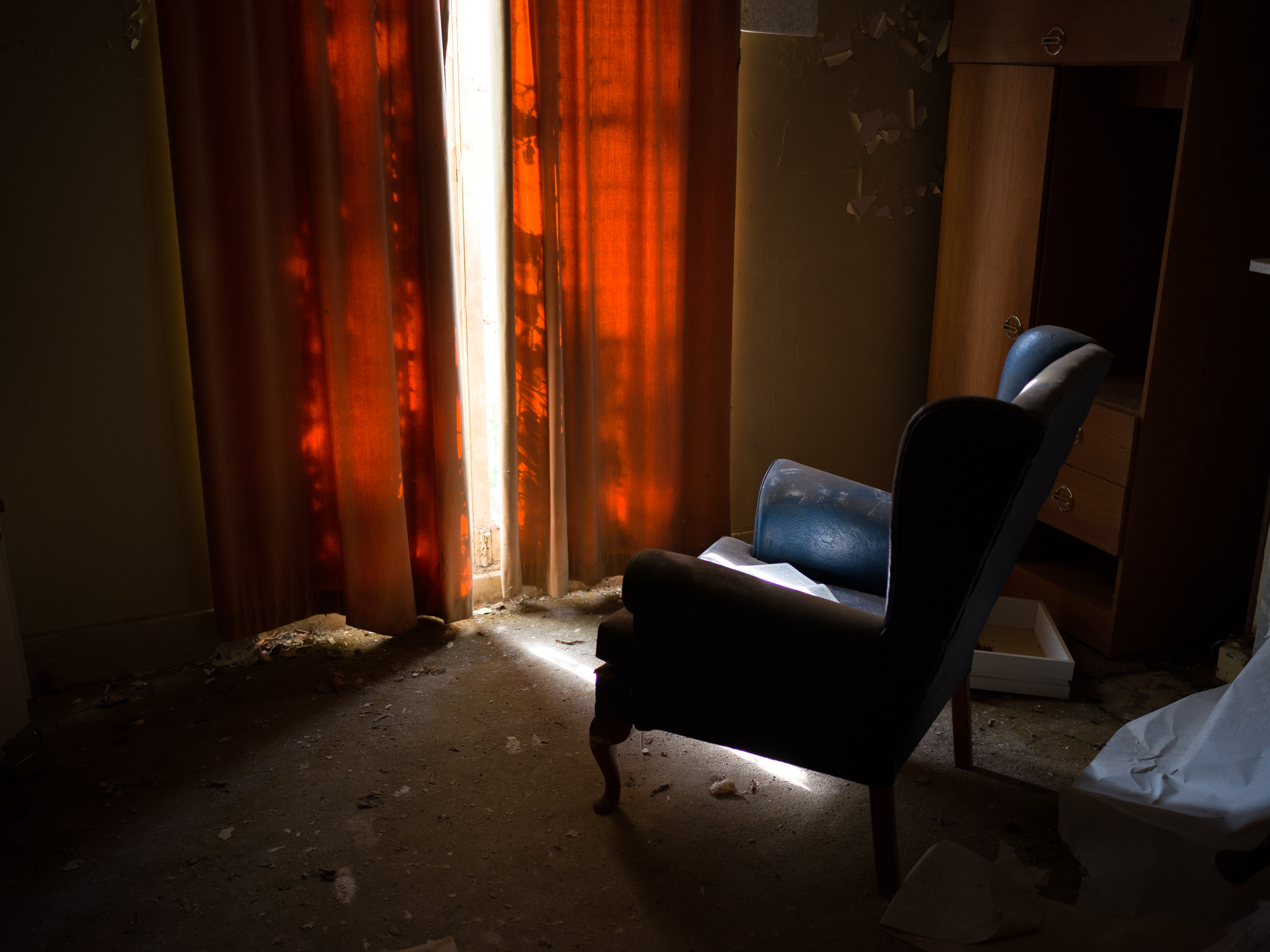 An old arm chairing front of a window with light illuminating an orange curtain