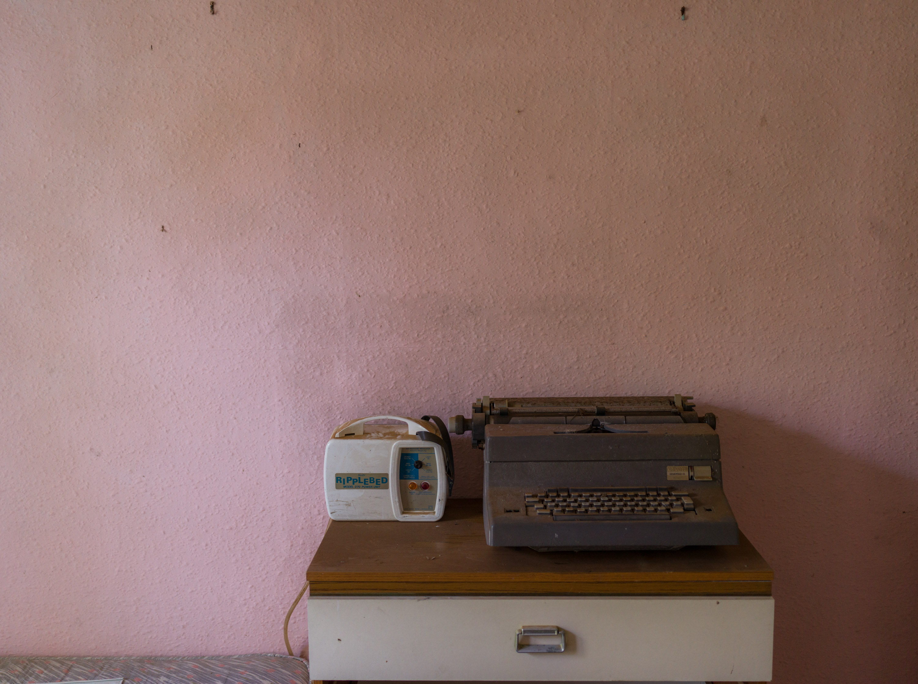 A typewriter on a chest of drawers behind a pink wall