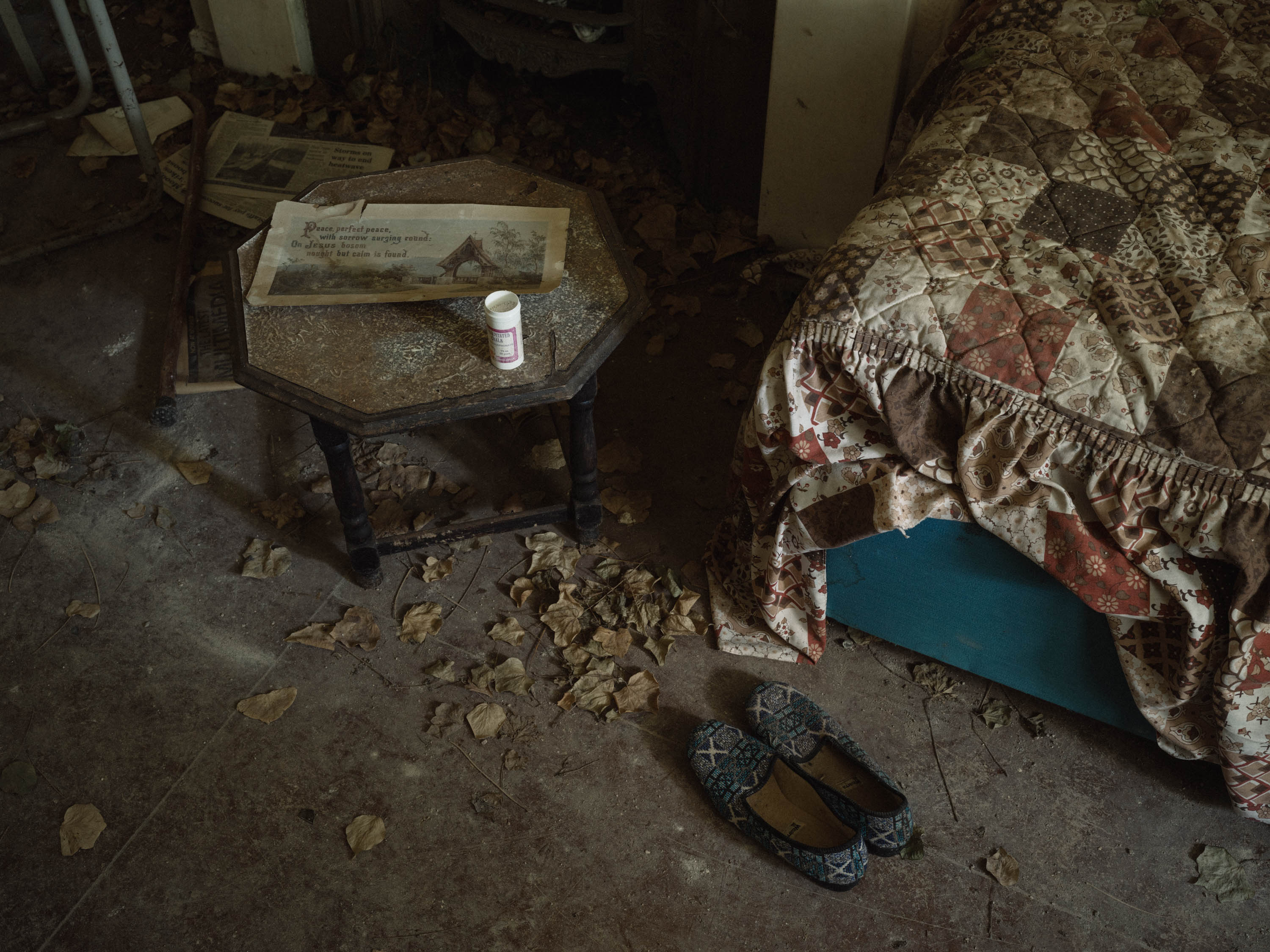 Corner of a bed some slippers and a a pill jar on a bedside table