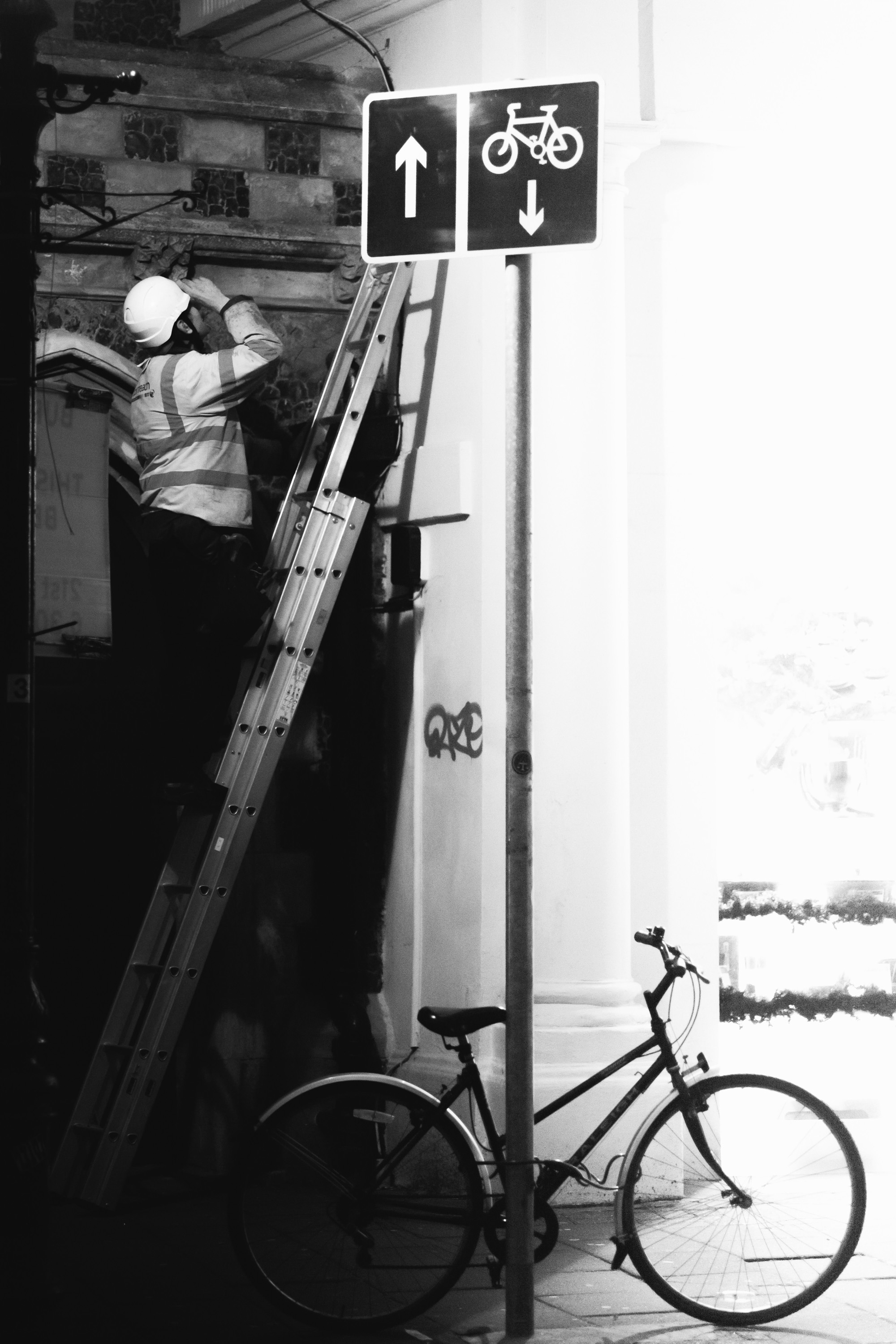 A person on a ladder looking at a signpost with a bike in foreground