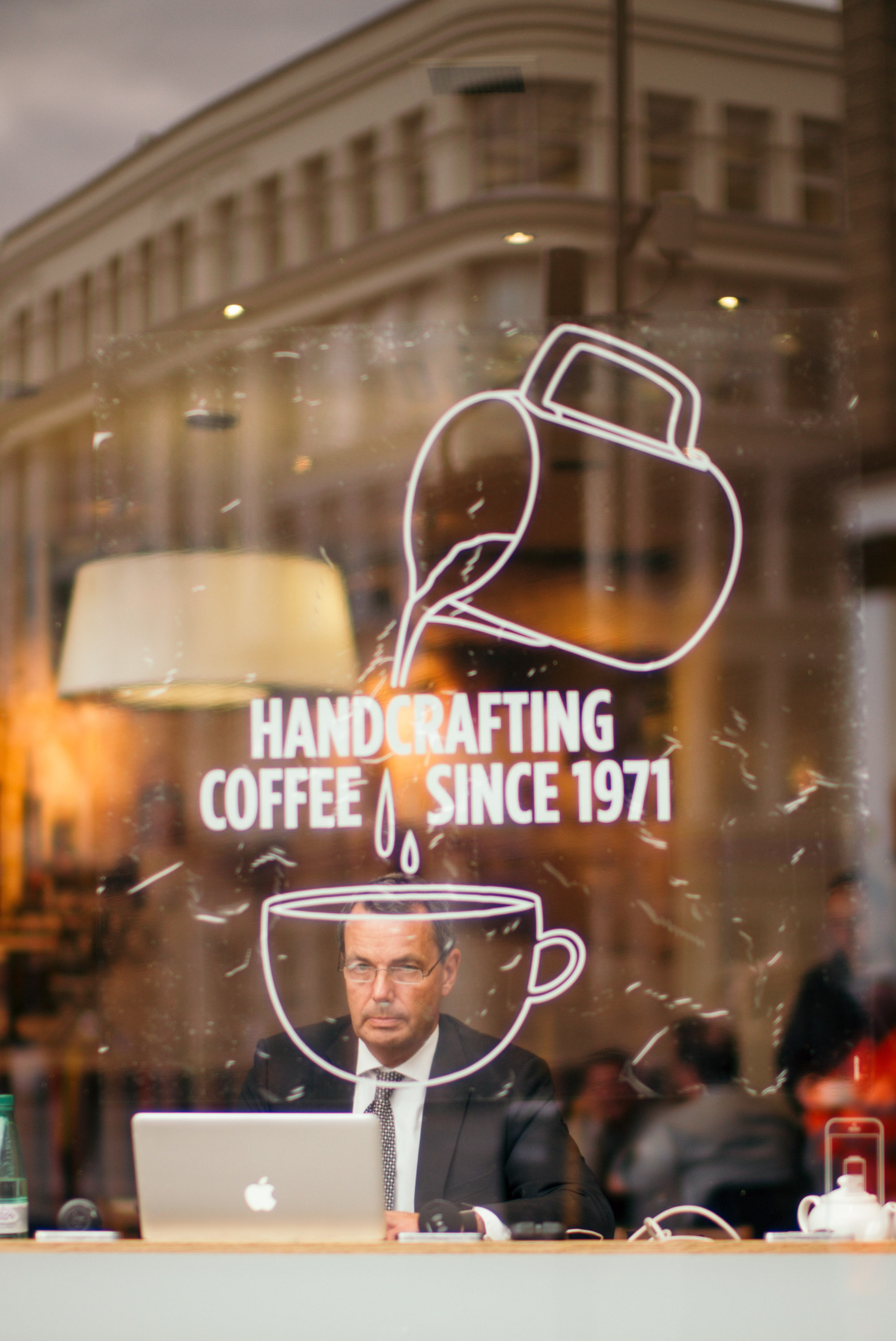 A person in a suit with a laptop that looks through the window with a coffee cup sign imprinted on it
