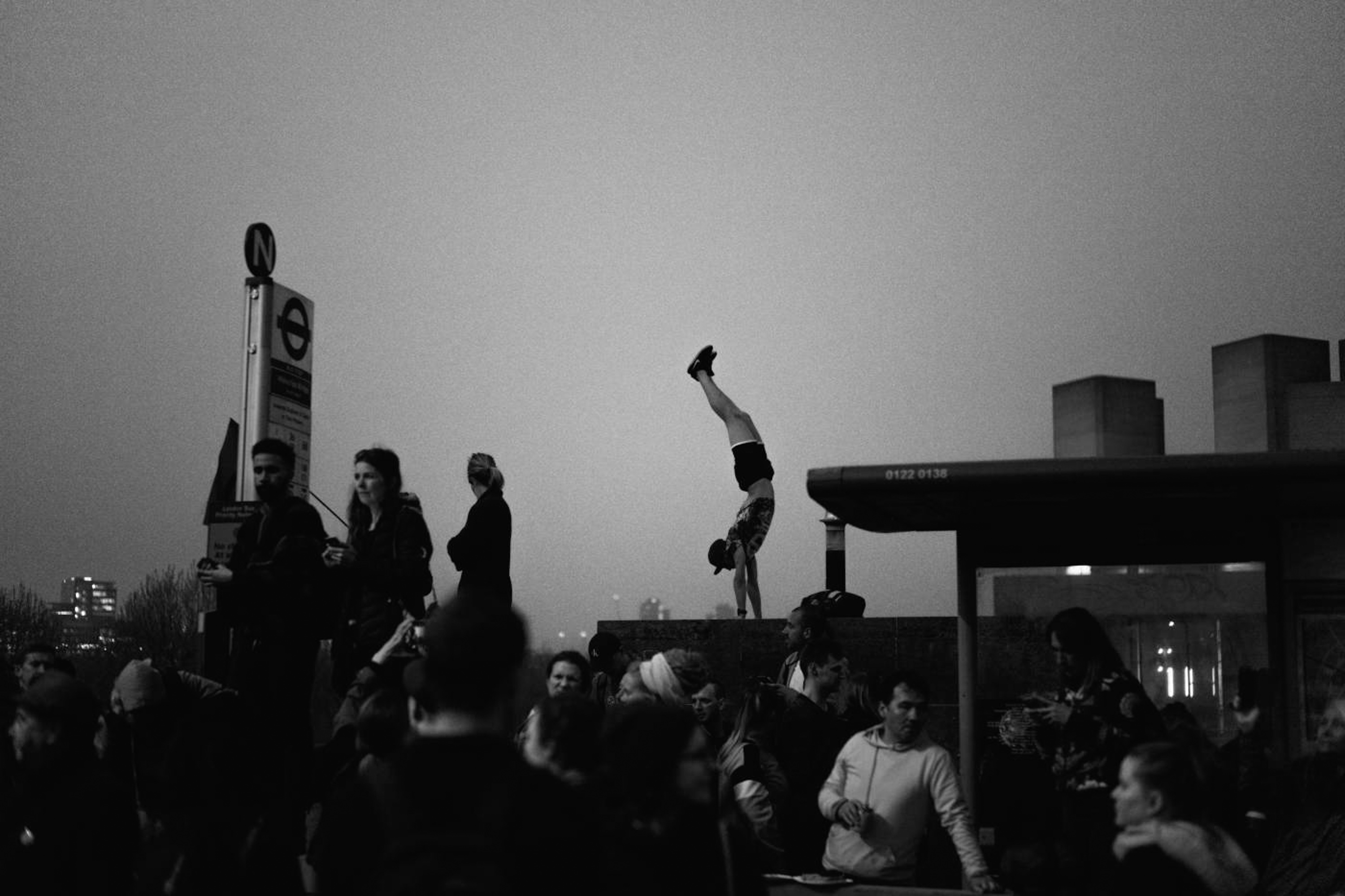 Black-and-white photo of a man doing a handstand in a crowd in London