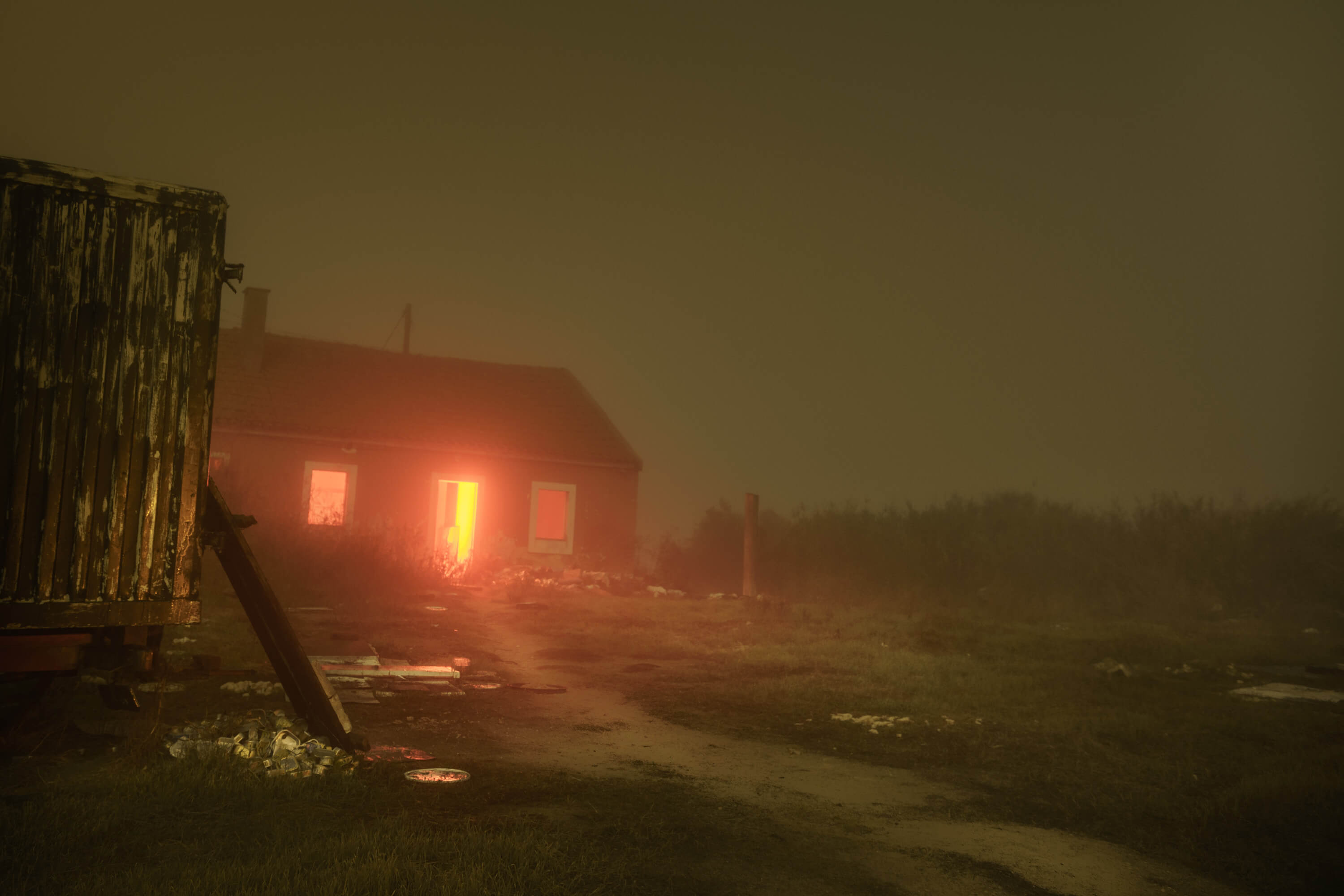 a house in fog with a rd light emanating from the doorway