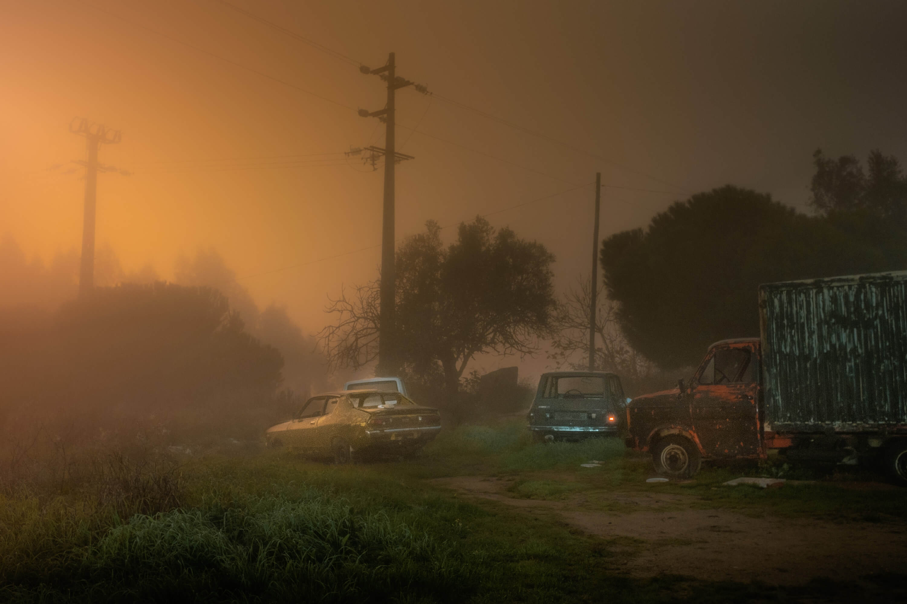 a foggy scene at dusk with cars scattered in a yard