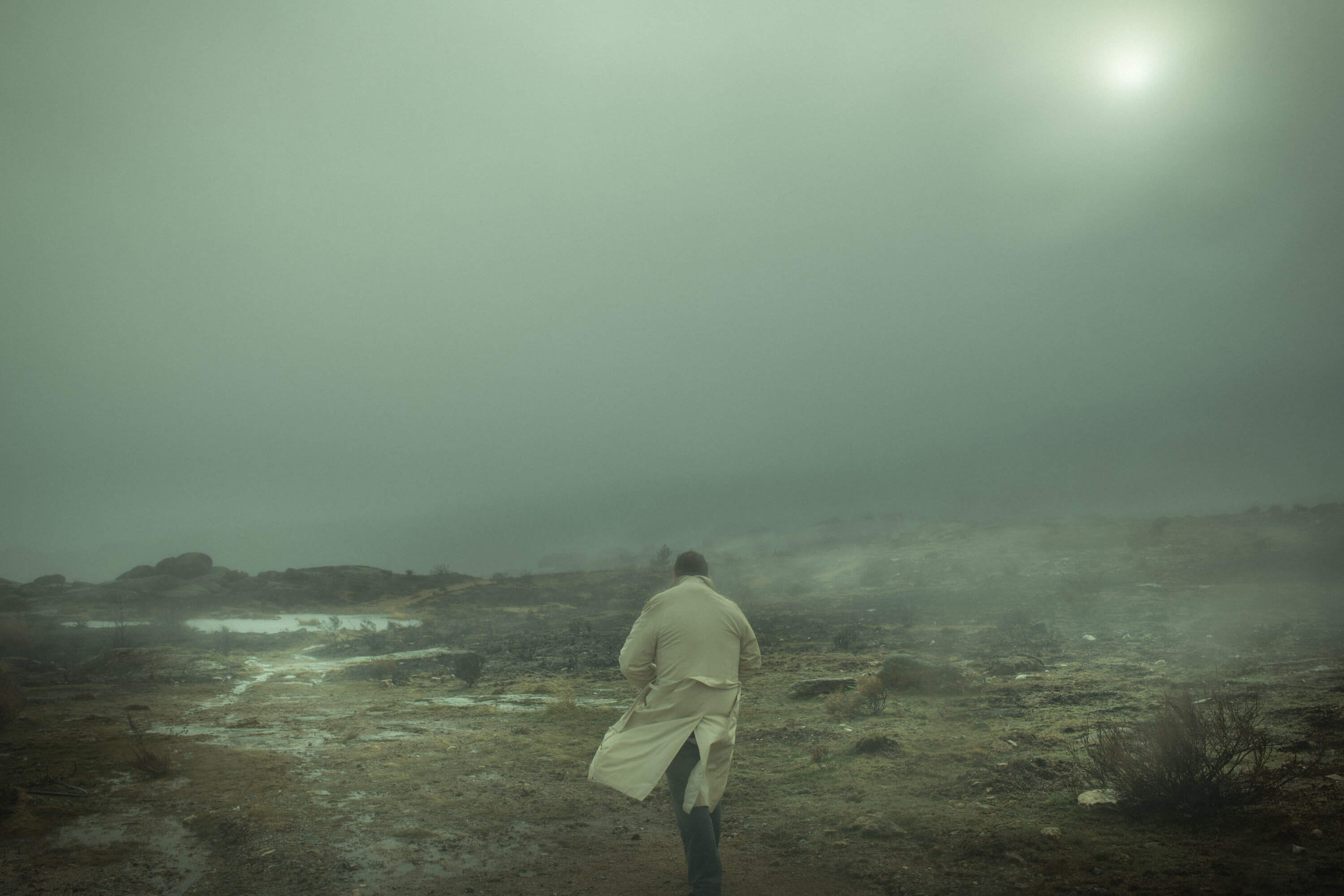 a misty shot of a man in a trench-coat running in the distance