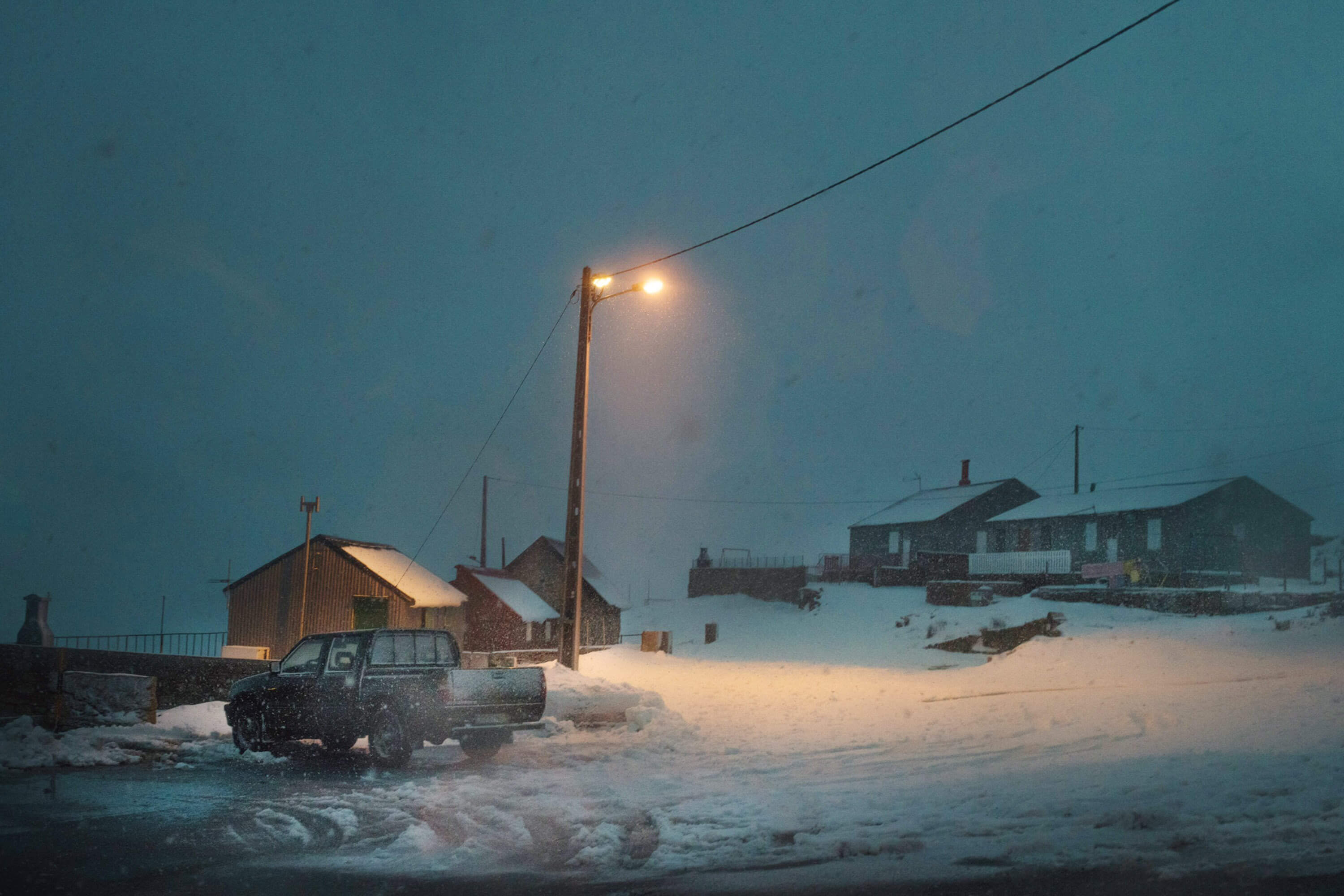 a snowy landscape of car under a street lamp