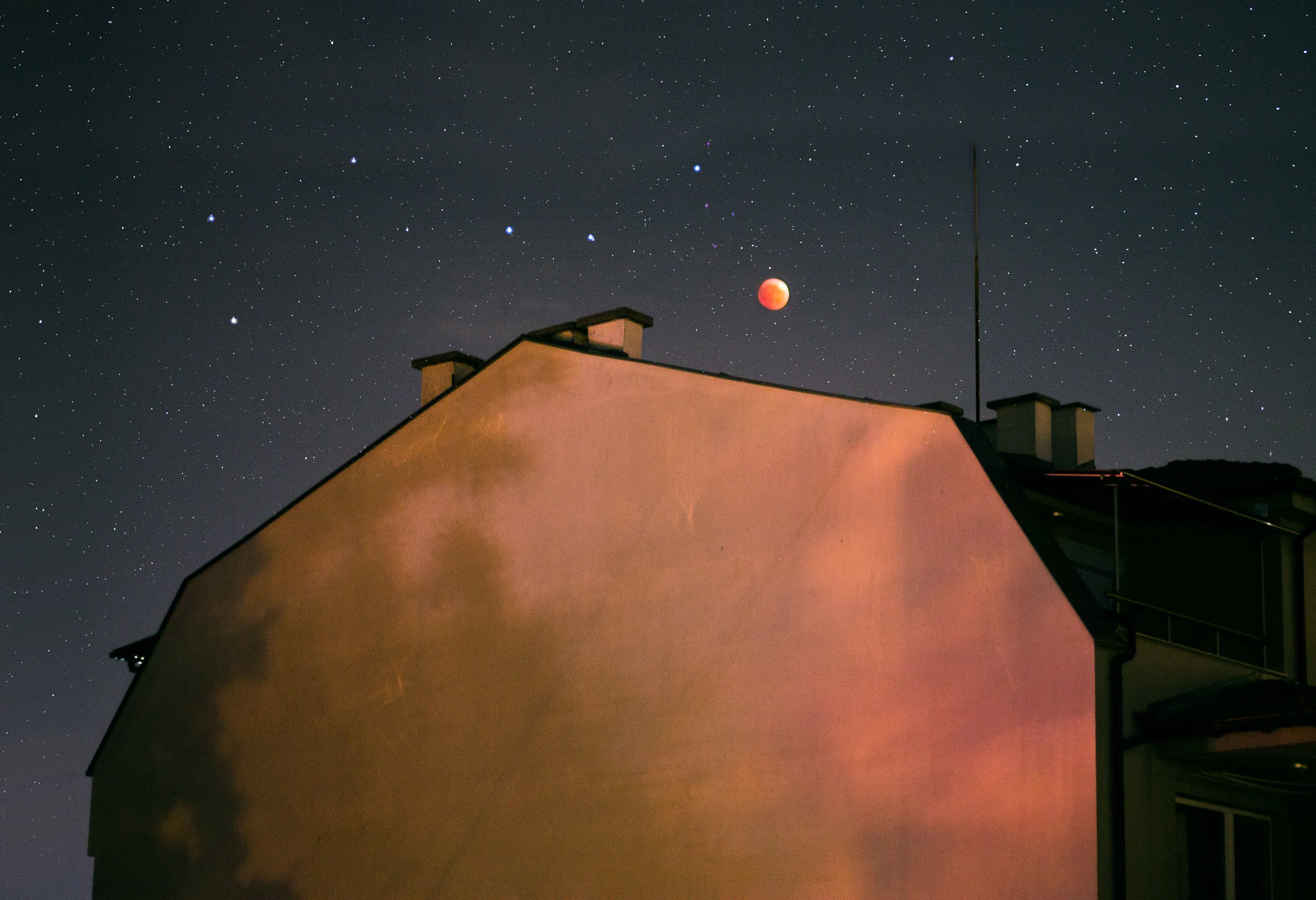 A blood red moonlit sky behind a building, shadows gently dancing on the building wall.