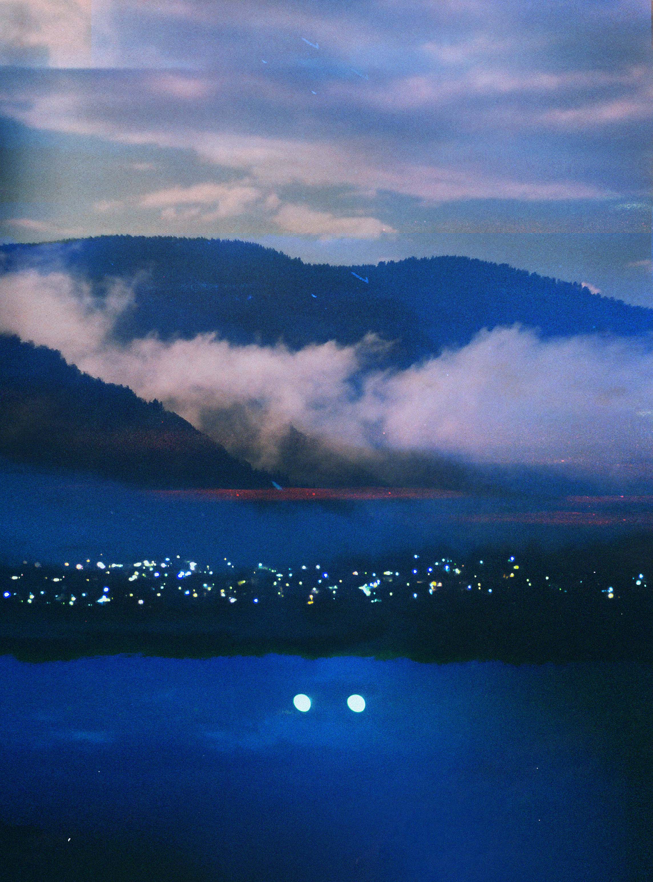 A predominantly blue photo of clouds timidly balancing above a town.