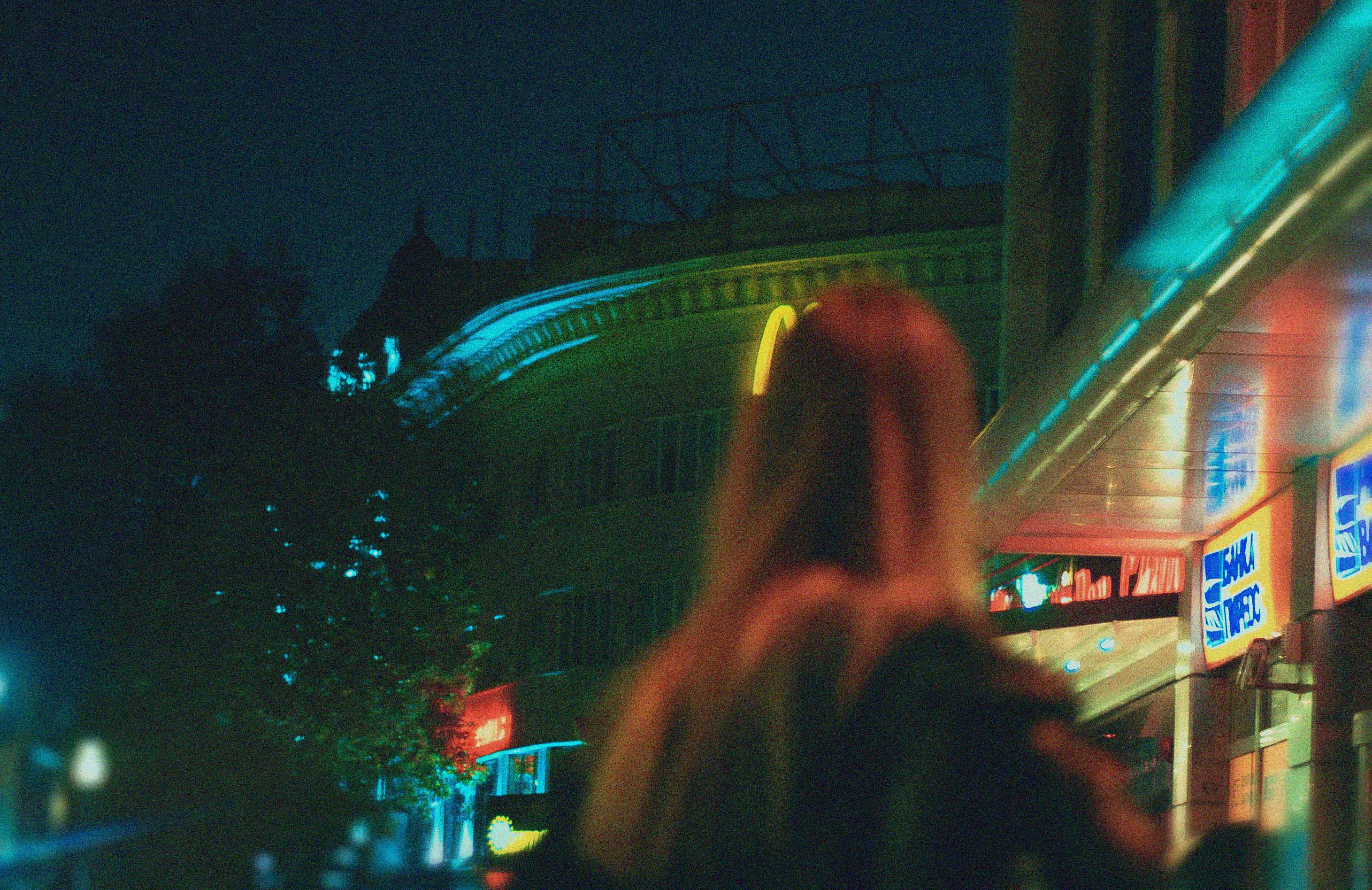A girl outside at night, looking longingly at a fast food sign in the distance