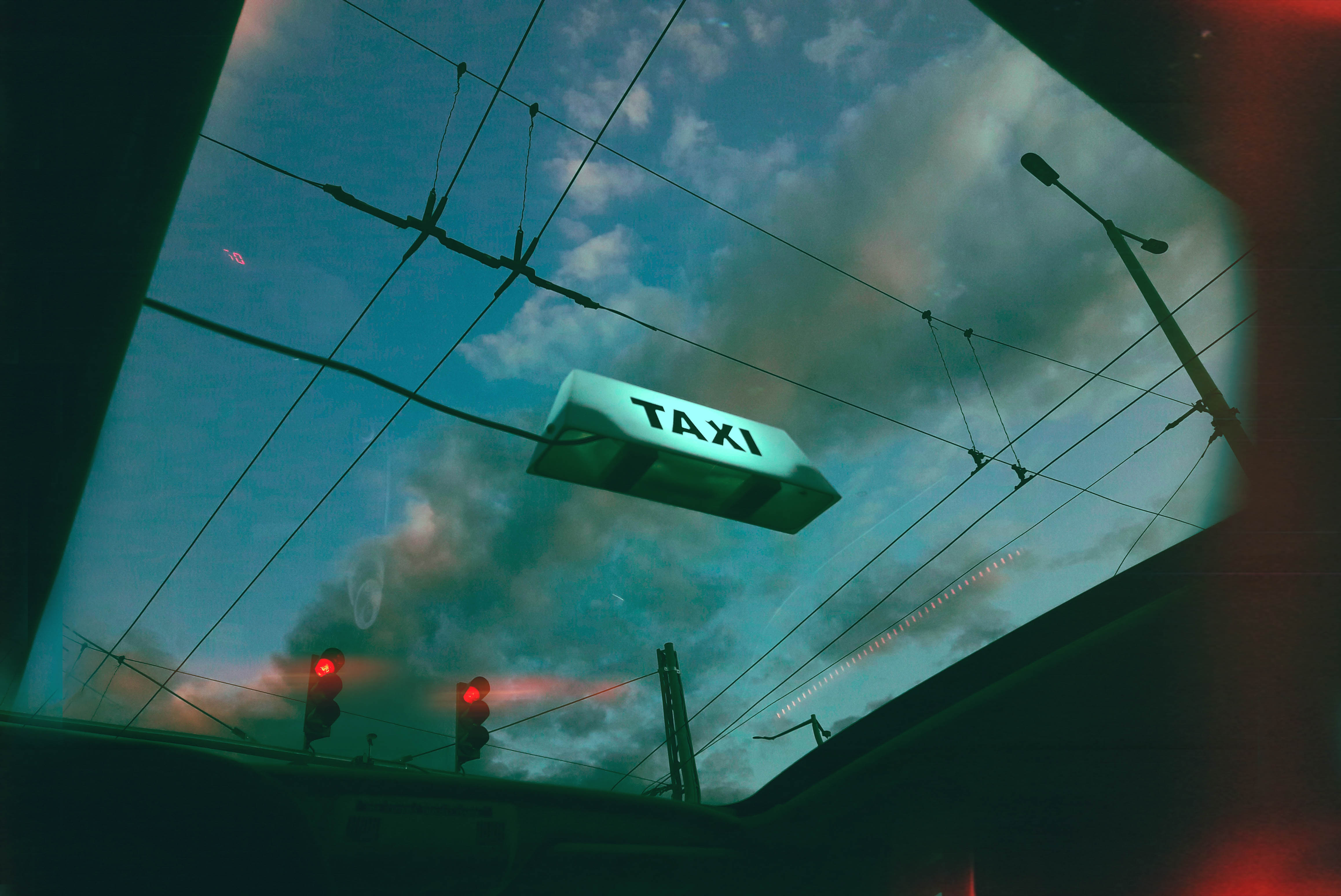 A taxi sign as viewed by the passenger inside the car against a dusk sky.