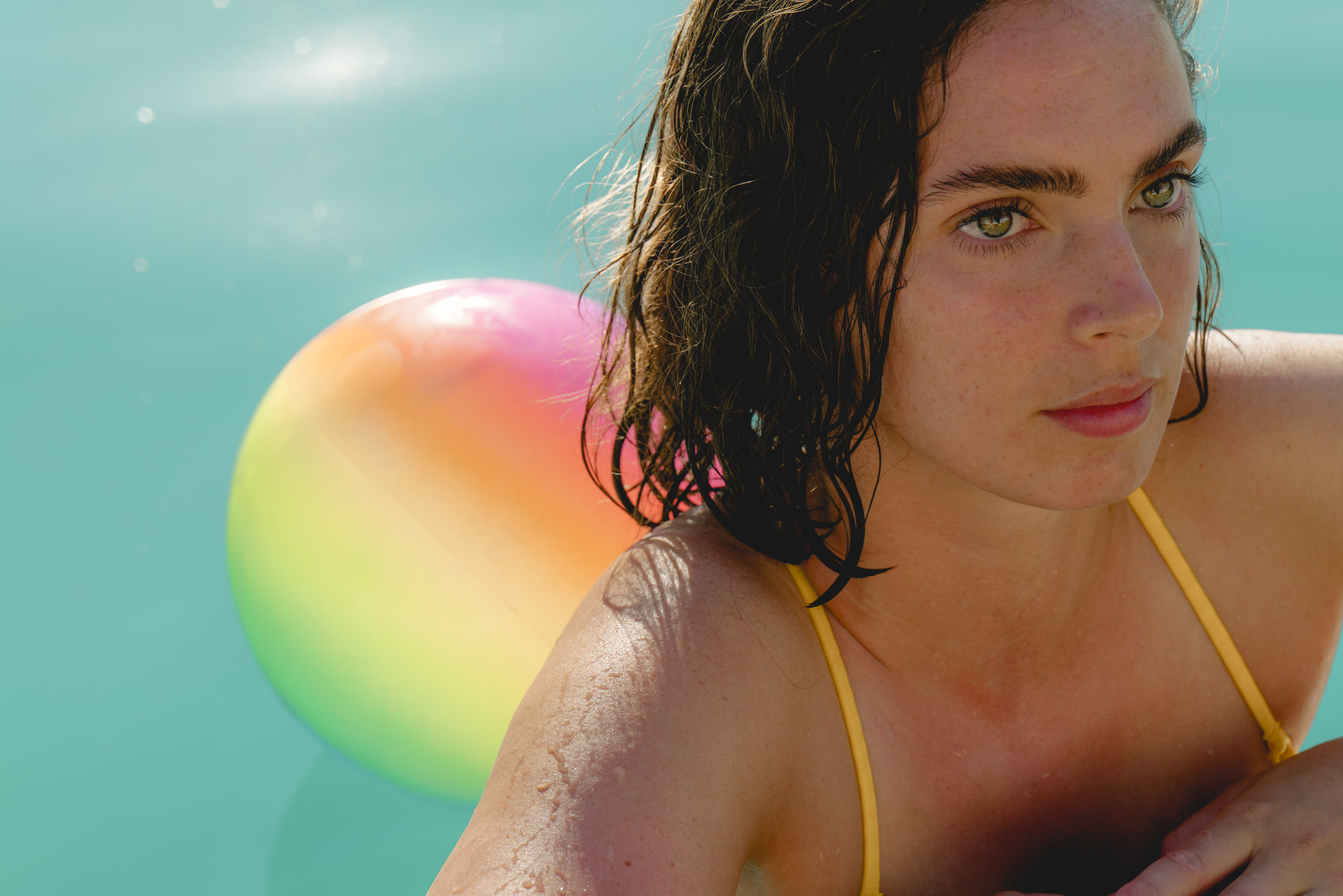 A woman looking stern in a swimming pool with a beach ball next to her
