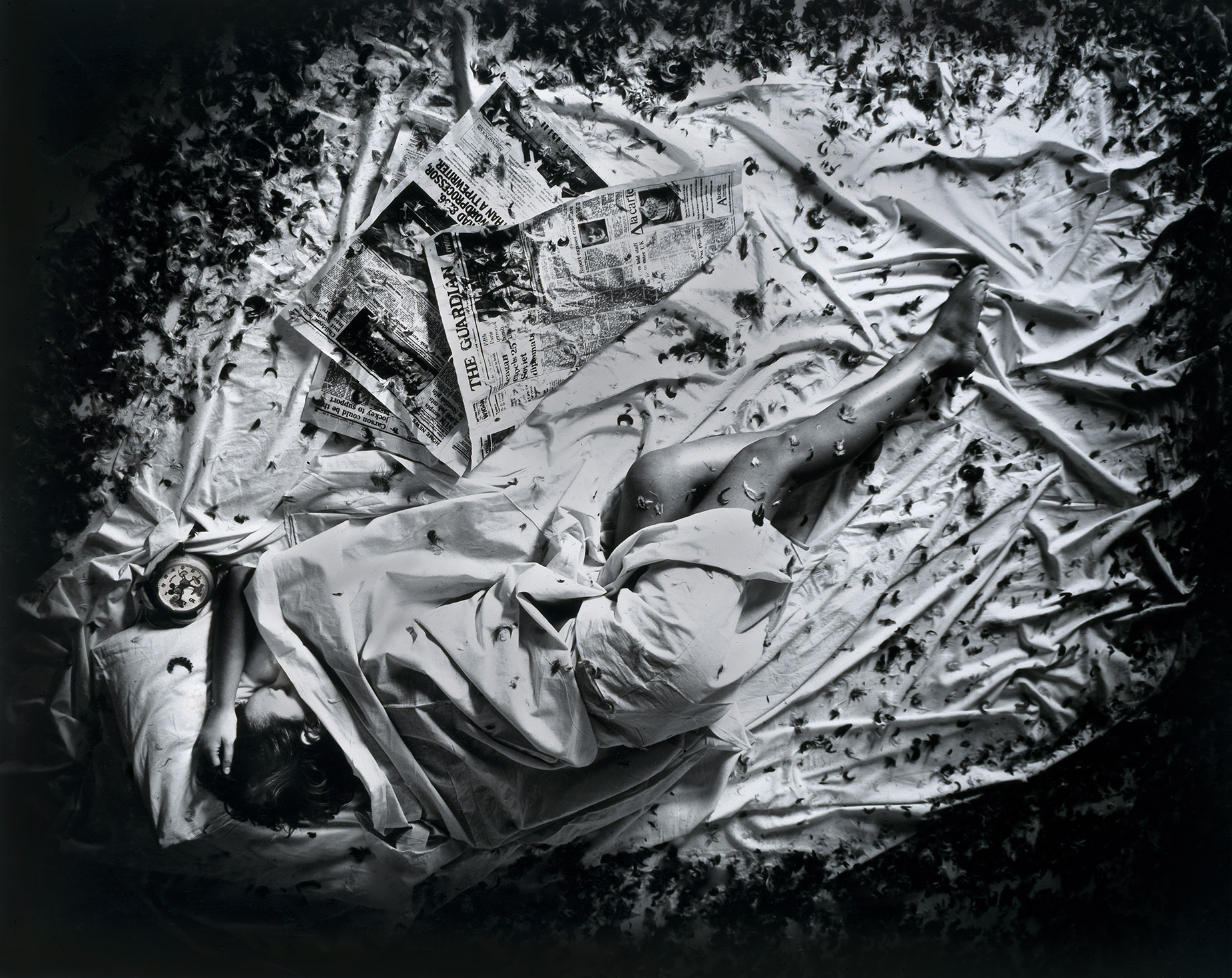 Black-and-white photo of someone lying on a bed with a newspaper
