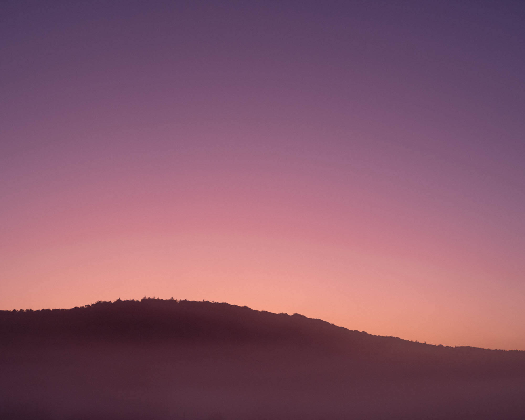 Silhouette of a hill at dusk with a lovely sunset gradient of pink and purple