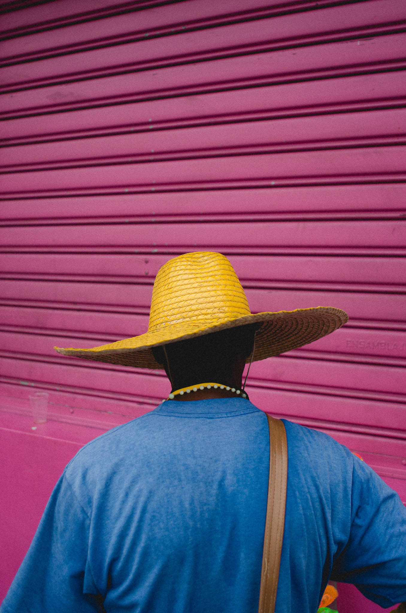 Street shot of a person wearing a bright yellow hat with a pink background